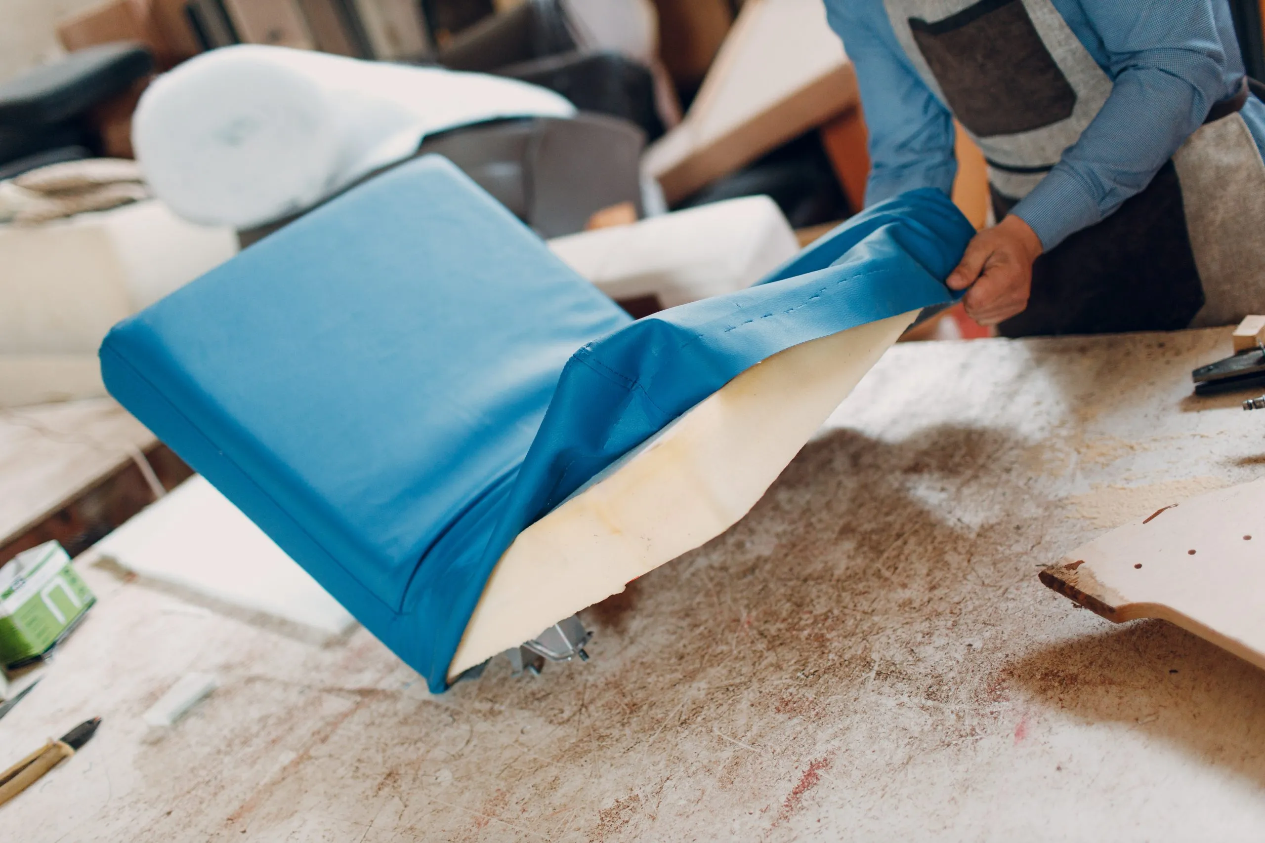 Tapissier agrafant un tissu neuf sur l'assise d'un fauteuil
